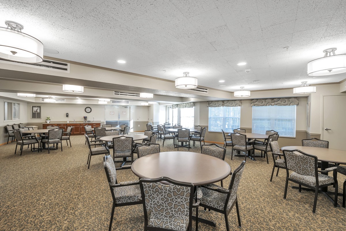 A spacious dining area featuring multiple tables and chairs, with ample lighting and carpeted floors.