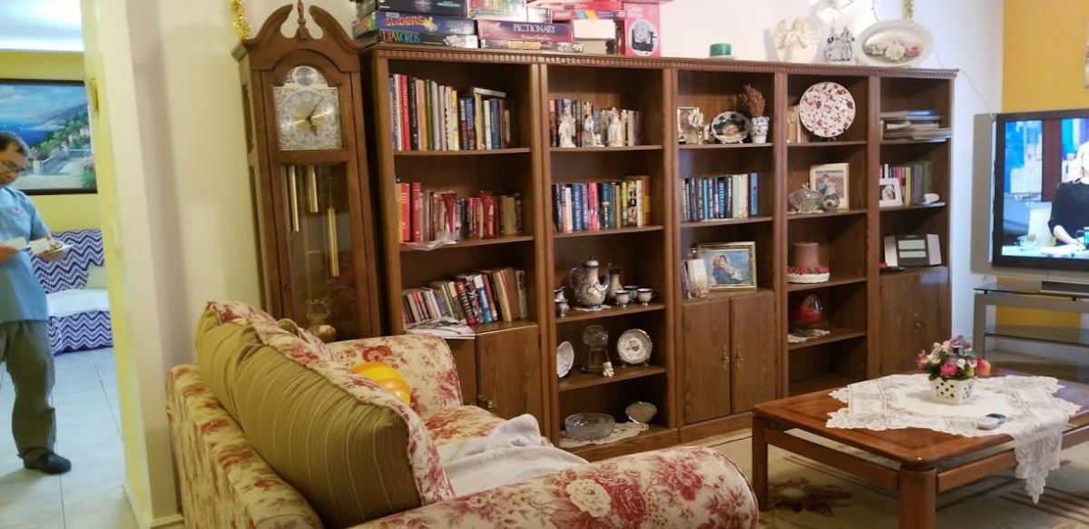 A cozy living room featuring bookshelves filled with books and collectible items, alongside a floral-patterned couch.