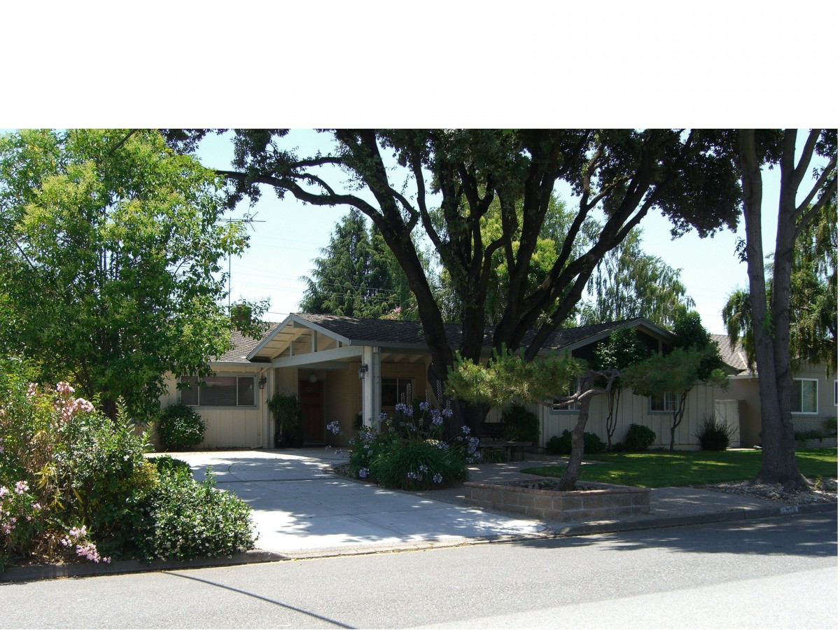 A suburban house with a driveway and large trees in the front yard.