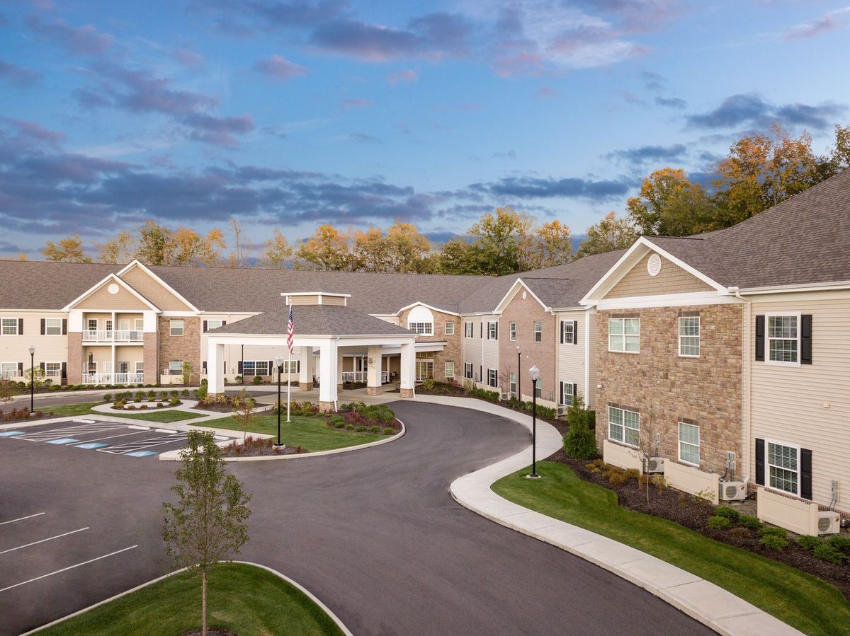 A large residential building with a curved driveway, surrounded by trees under a cloudy sky.