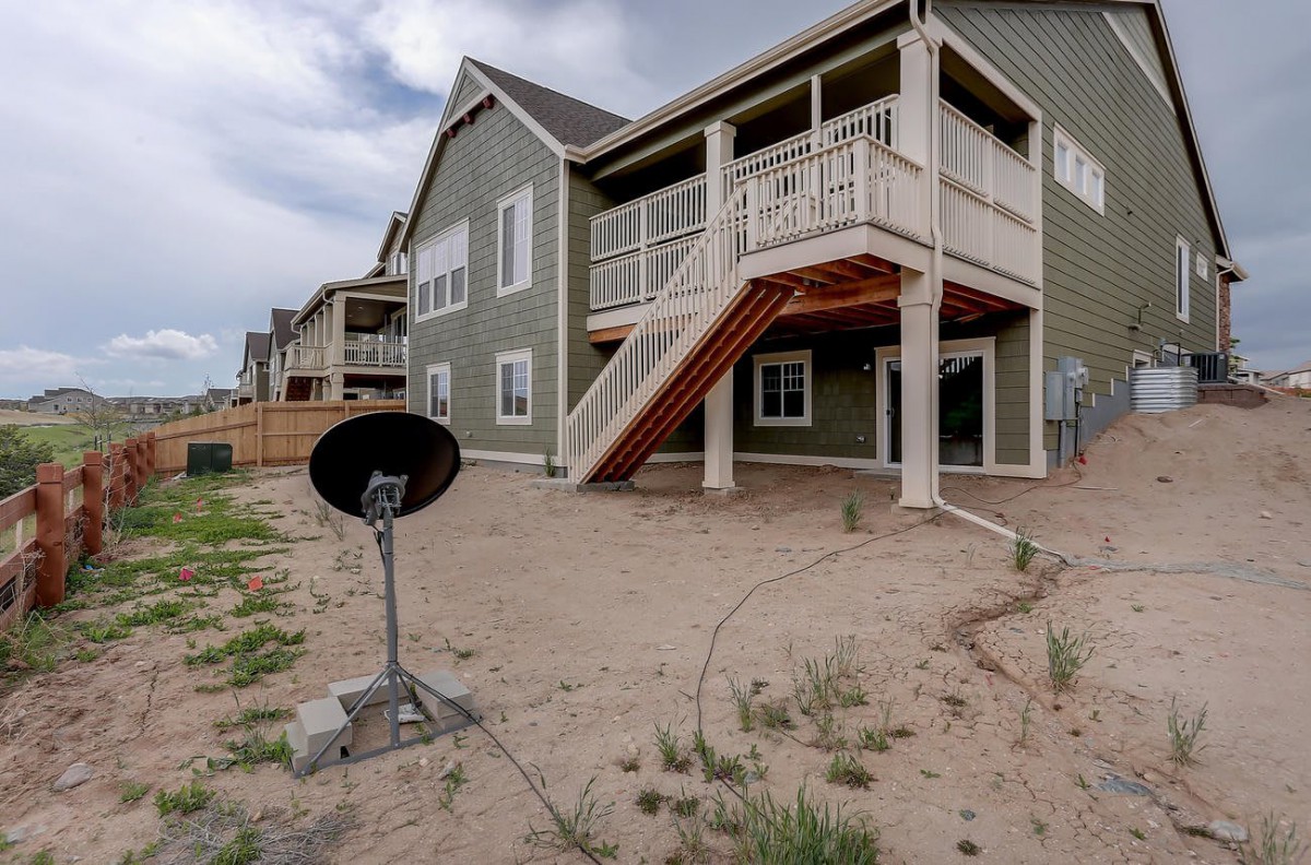 A modern house with a wooden staircase leading to the backyard and a satellite dish on the ground.