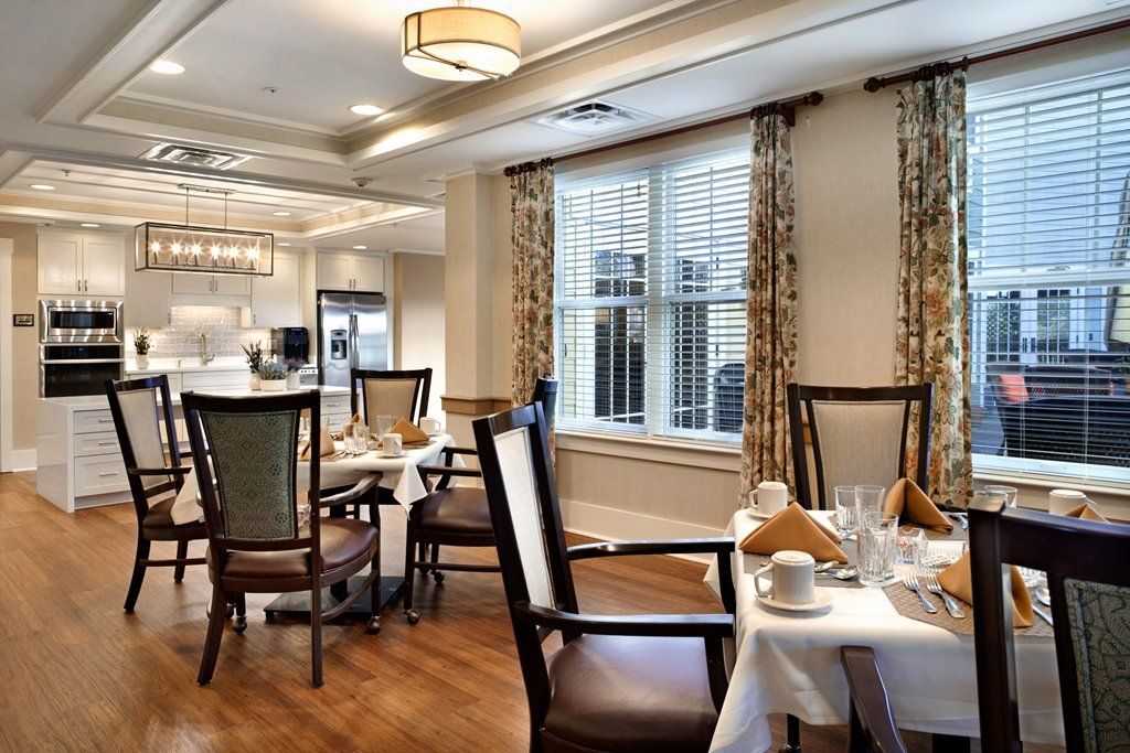 An elegant dining room with neatly arranged tables and chairs, featuring a window with curtains.