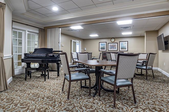 A well-lit dining area with tables and chairs, featuring a piano and framed artwork on the walls.