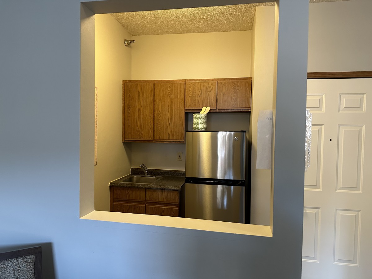 A compact apartment kitchen with a stainless steel refrigerator and wooden cabinets.