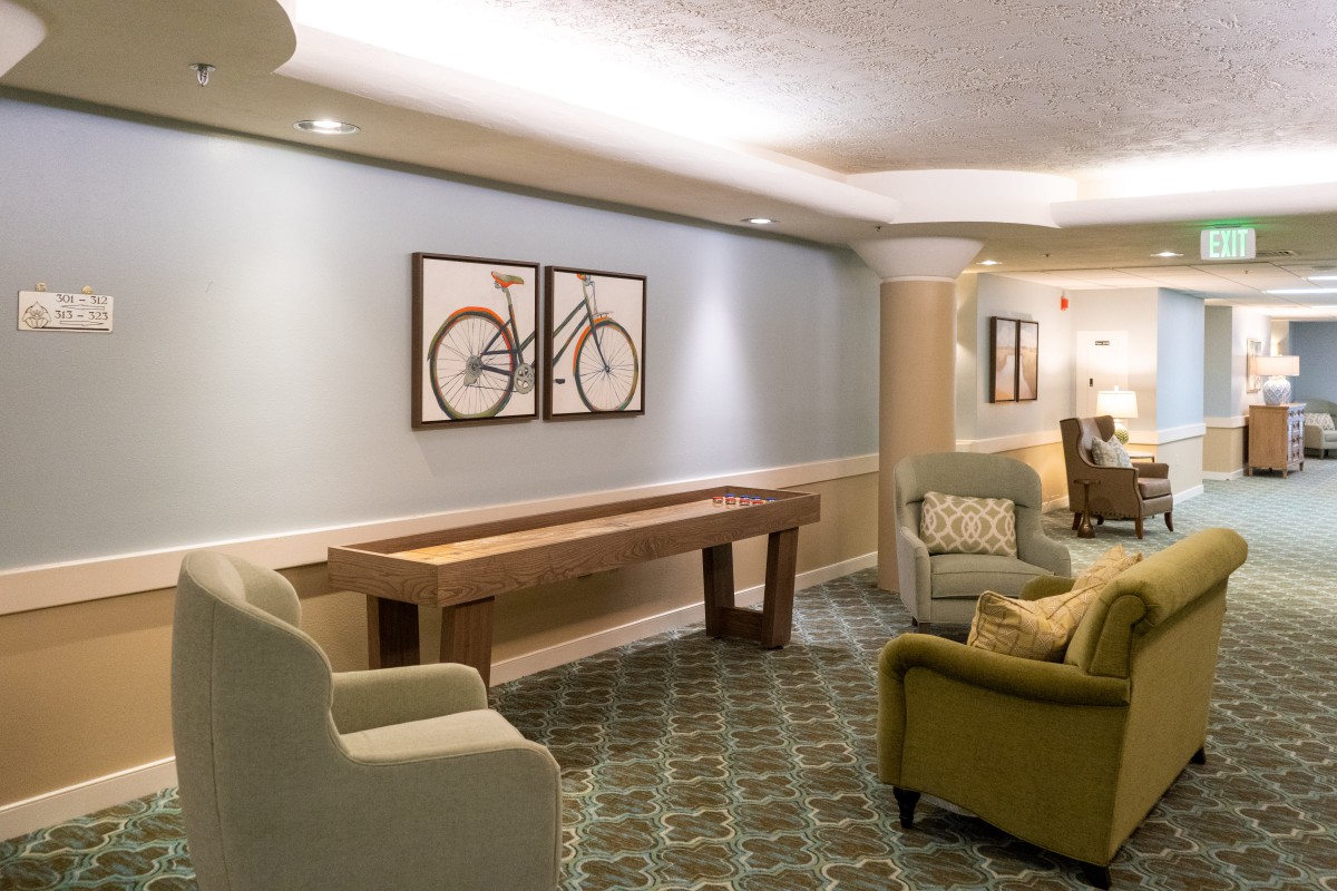 A cozy living room with comfortable seating, a shuffleboard table, and bicycle artwork on the wall.