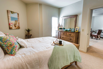 A cozy and well-decorated bedroom featuring a comfortable bed with a light green throw and a wooden dresser with a mirror.