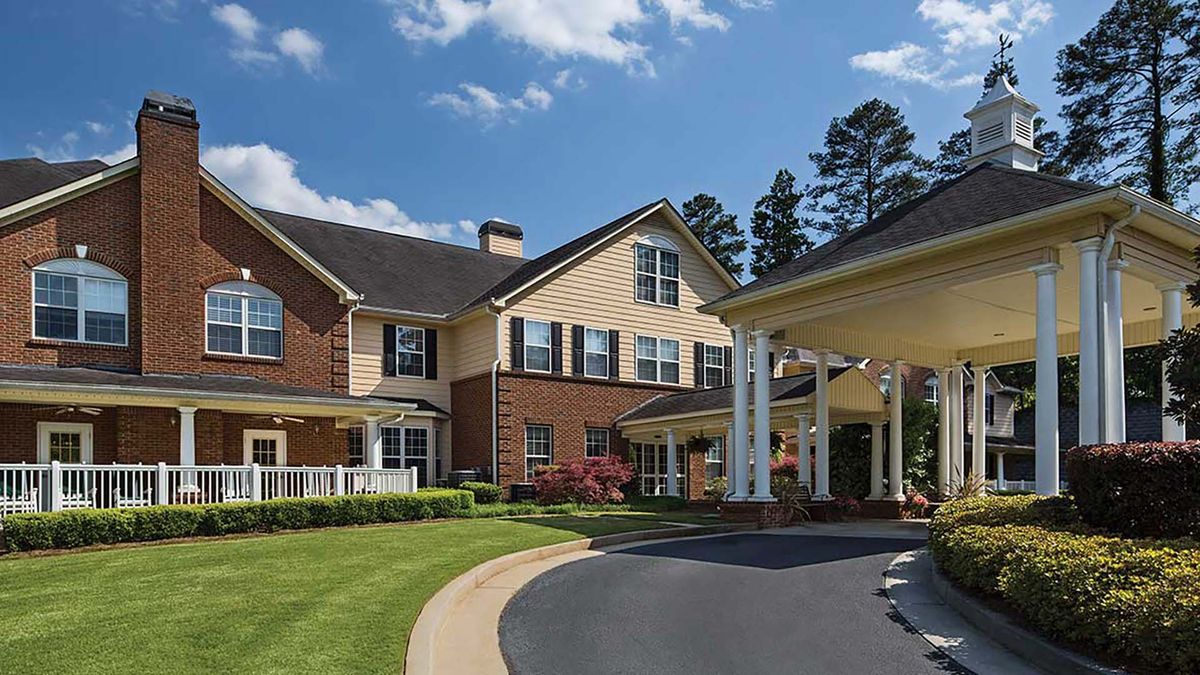 A large residential building with brick and siding exterior, surrounded by well-maintained landscaping and a curving driveway.
