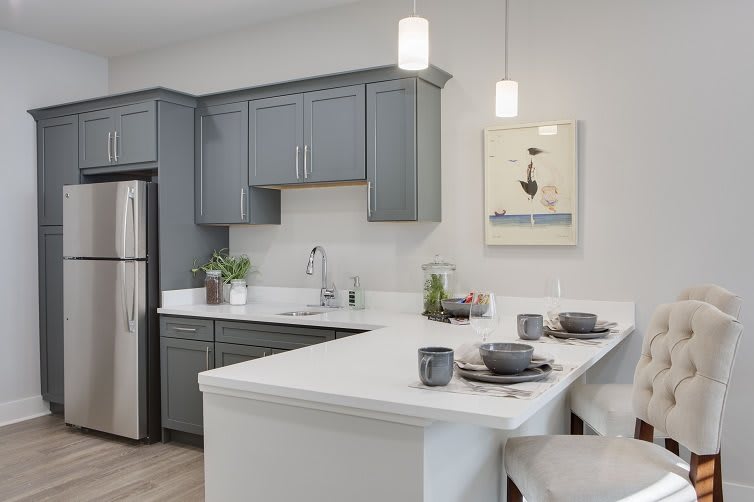 A modern kitchen with gray cabinets and a white countertop island, featuring stainless steel appliances and minimalist decor.