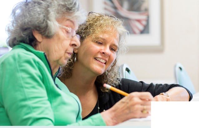 An elderly woman receiving assistance with writing from a caregiver.