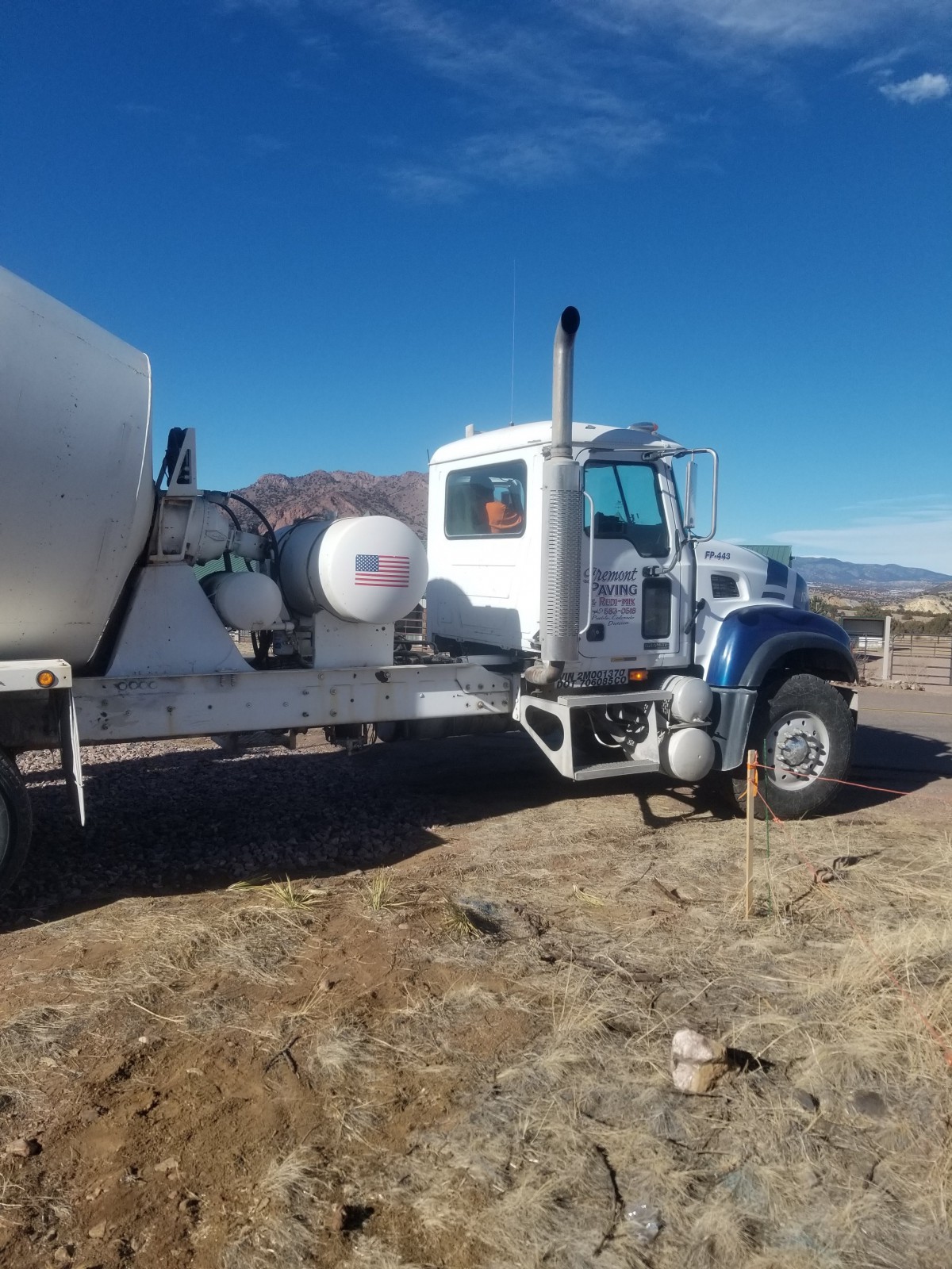A cement mixer truck parked on a construction site under a clear blue sky.
