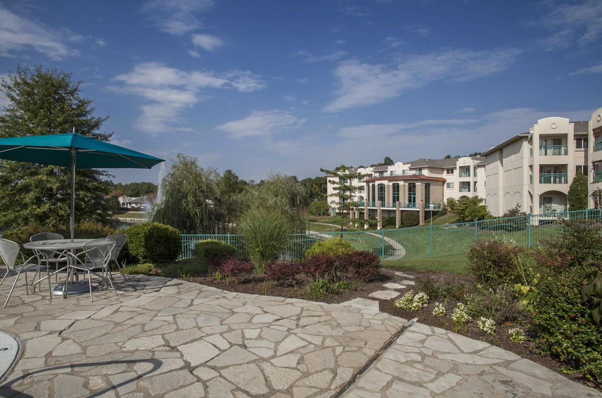 A scenic view of a landscaped garden with a stone patio, overlooking modern buildings under a clear blue sky.