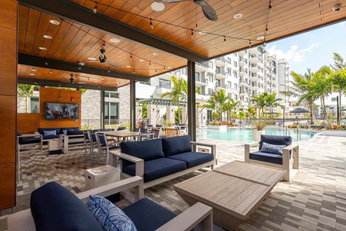 A modern outdoor patio area with comfortable furniture and a view of the pool in an apartment complex.