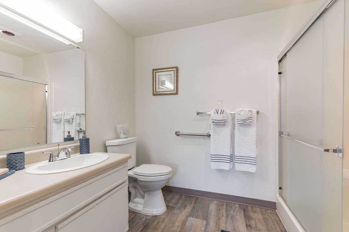 A clean and minimalistic bathroom featuring a toilet, sink with a mirror, shower stall, and neatly hung towels.
