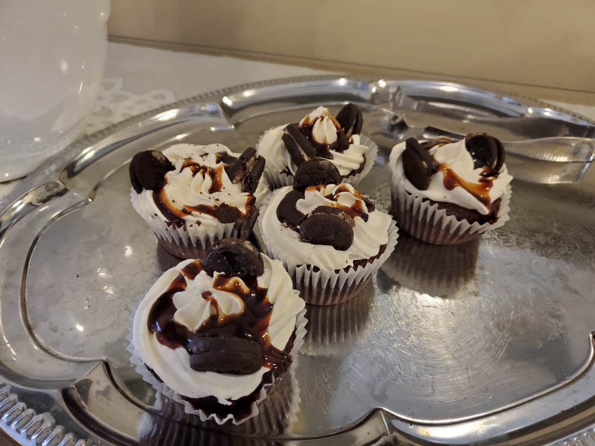 A tray of chocolate cupcakes topped with whipped cream and drizzled with chocolate sauce.