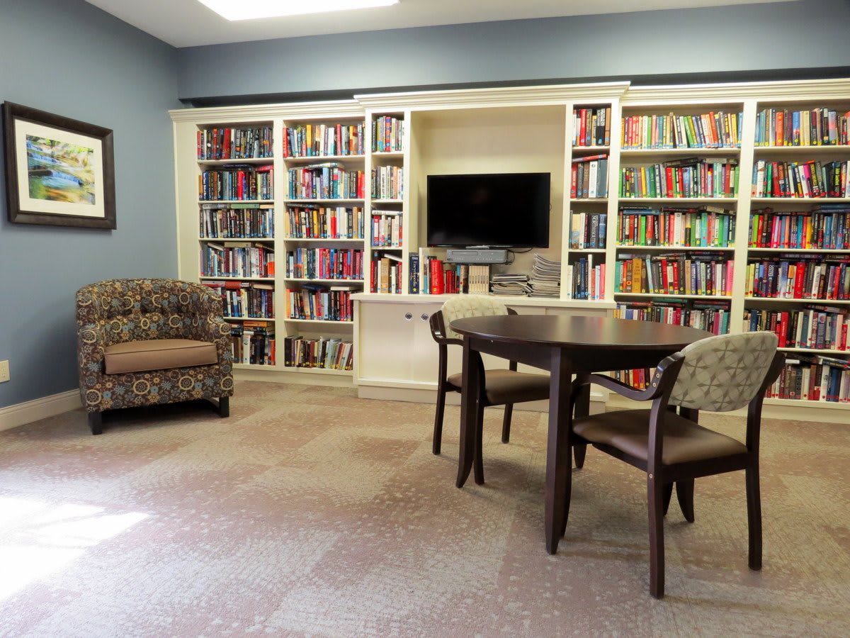 A cozy library room featuring bookshelves, a table with chairs, and a television.