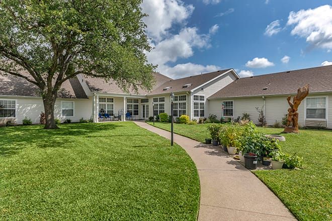 A suburban house with a well-maintained lawn and a garden pathway under a partly cloudy sky.