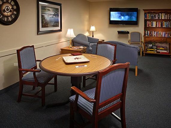 A cozy living room with a round table and upholstered chairs, featuring a television on the wall.