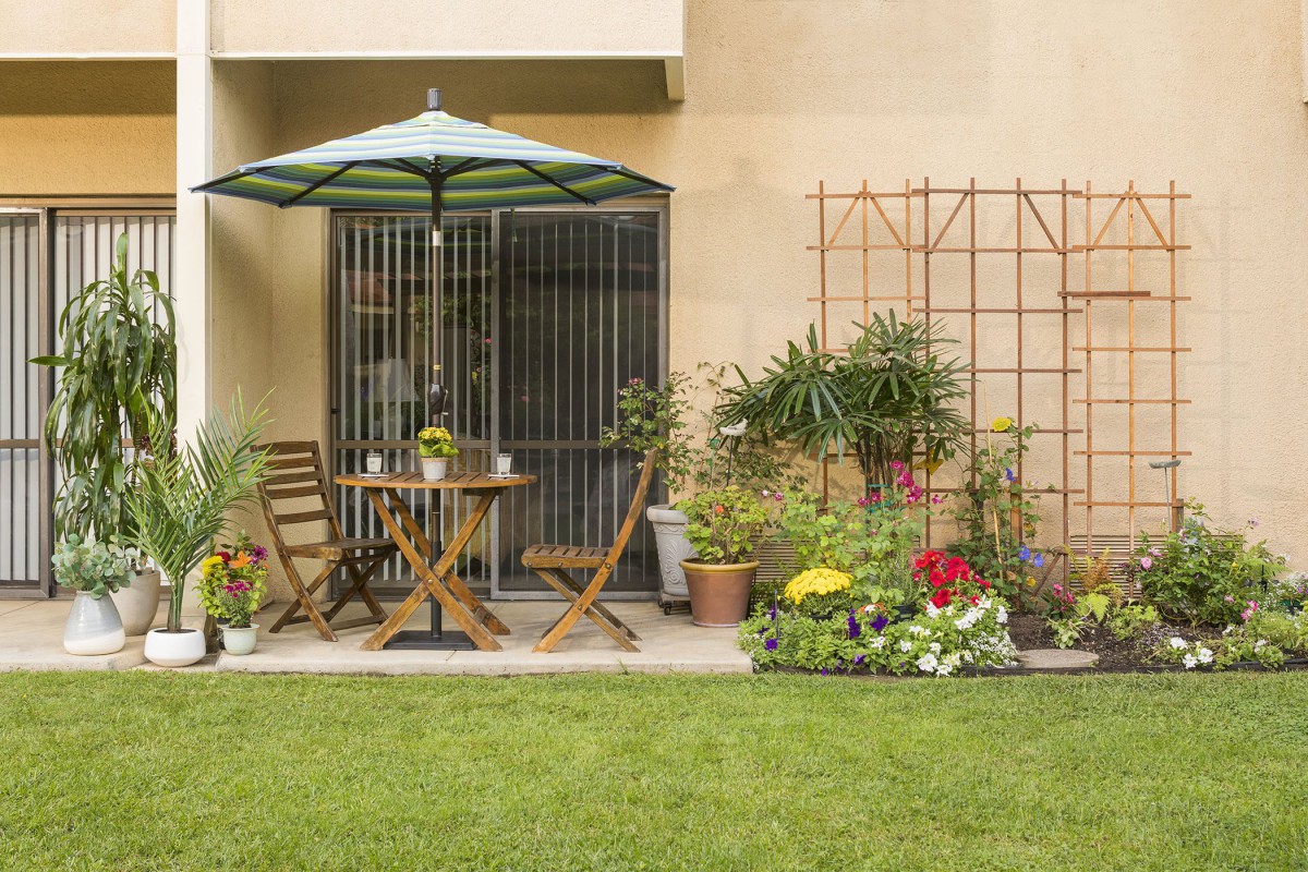 A cozy patio area with a table, chairs, and an umbrella, surrounded by a well-kept garden.