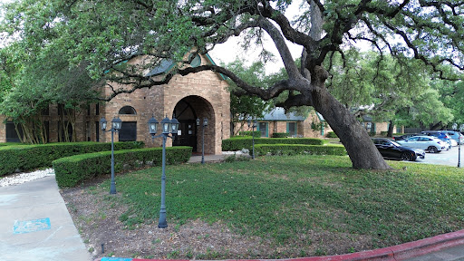 A charming building surrounded by lush greenery and mature trees.