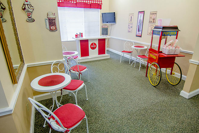 A vintage-style ice cream parlor with red and white decor, featuring tables, chairs, and a popcorn machine.