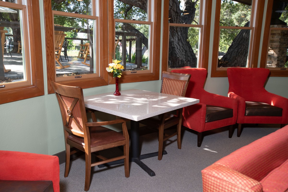 A cozy dining area with a table and chairs near large windows, decorated with a vase of flowers.