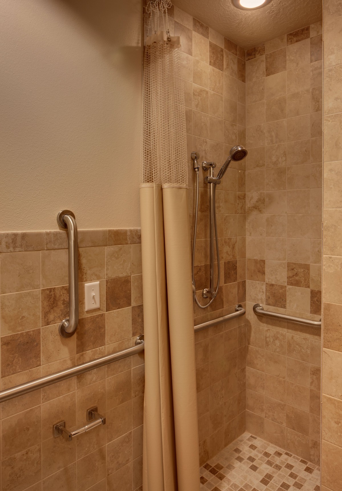 An accessible bathroom with tiled walls, a handheld showerhead, and grab bars.