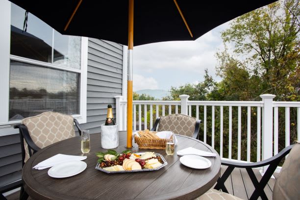 A cozy outdoor patio setting with a table under an umbrella, featuring champagne and a cheese platter.