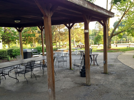 A serene picnic area under a wooden pavilion, surrounded by greenery.