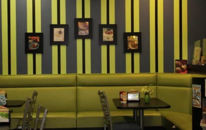 A modern restaurant interior with green and black striped walls, featuring framed artworks and cozy seating arrangements.