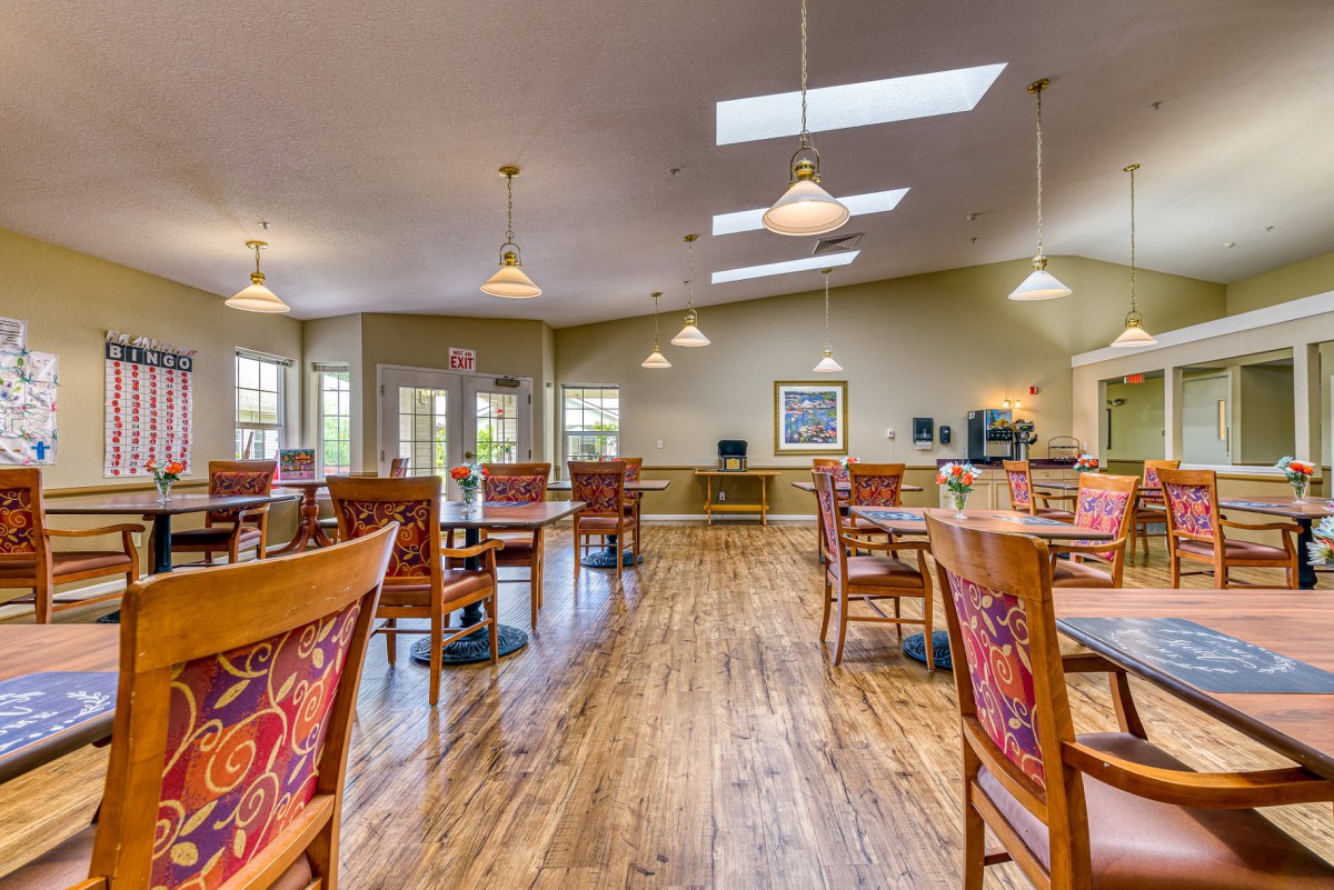 A spacious dining area with wooden floors and neatly arranged tables and chairs.