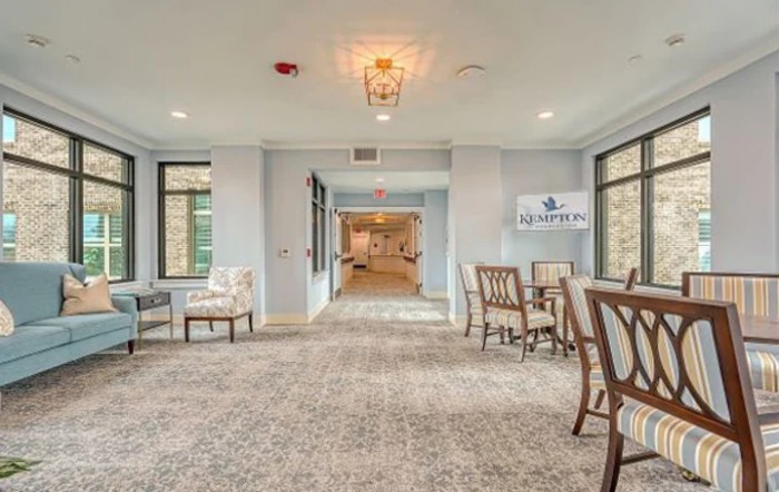 A spacious lobby area with chairs and tables, featuring large windows and carpeted flooring.