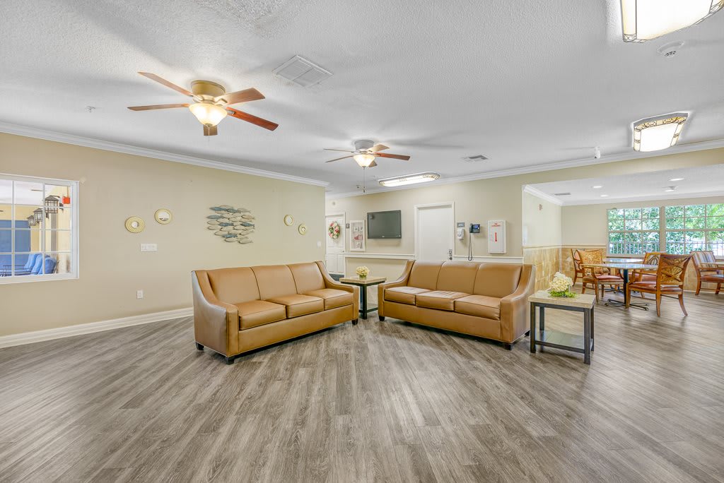A spacious living room with two brown sofas, wood flooring, and ceiling fans.