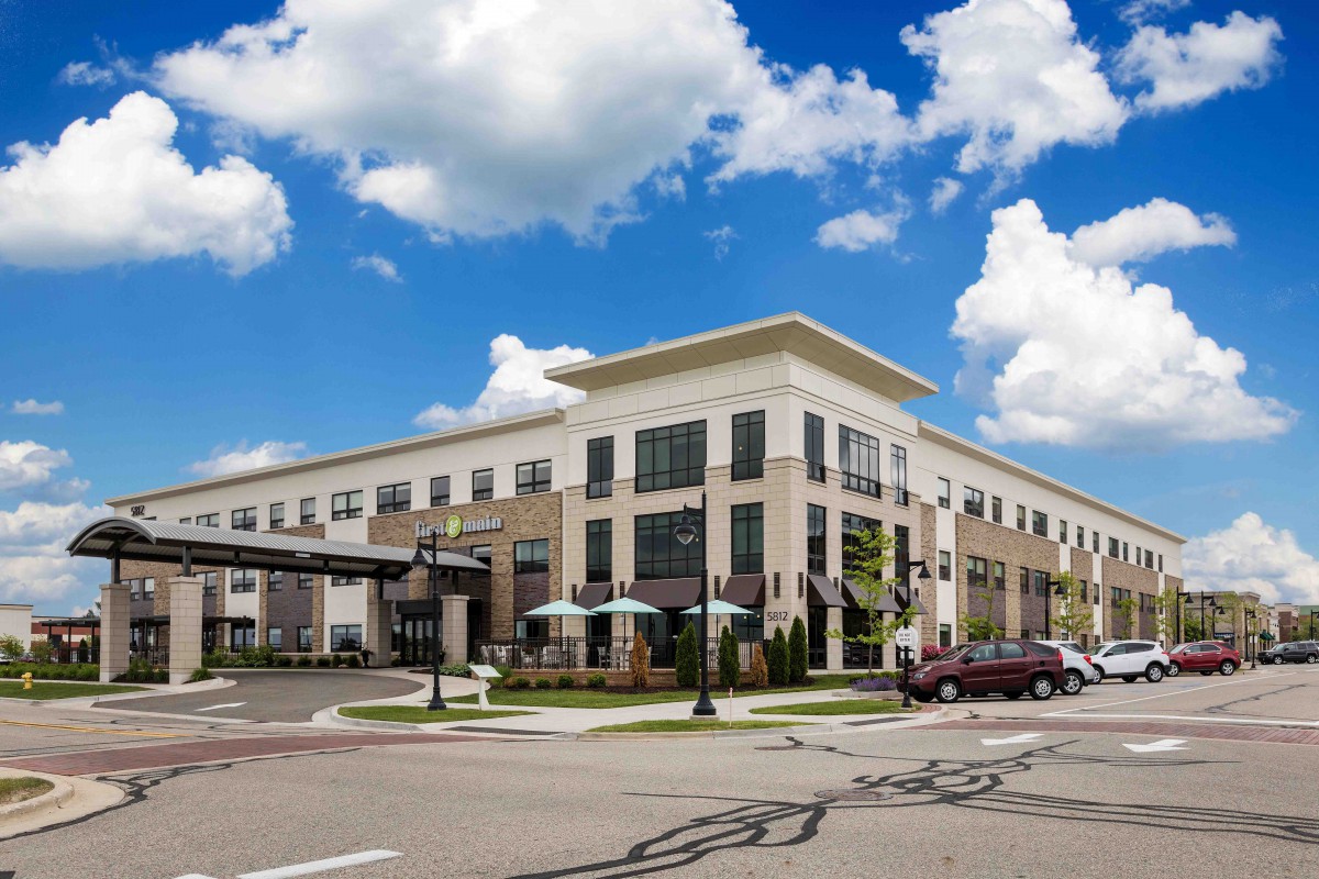 A modern commercial building under a blue sky with clouds, viewed from the street.