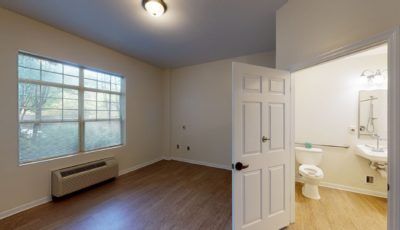 An empty room with wooden flooring and an adjoining bathroom.