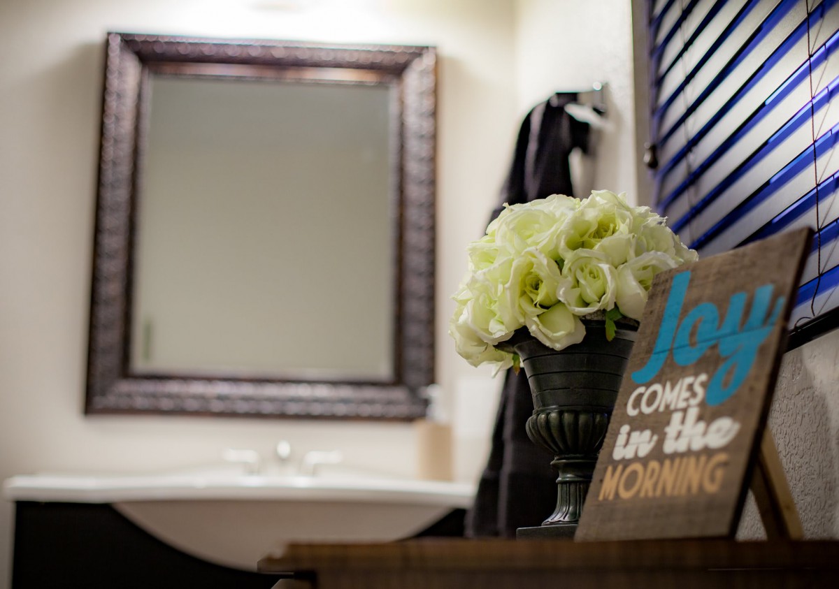 A bathroom featuring a mirror, flowers, and a decorative sign.