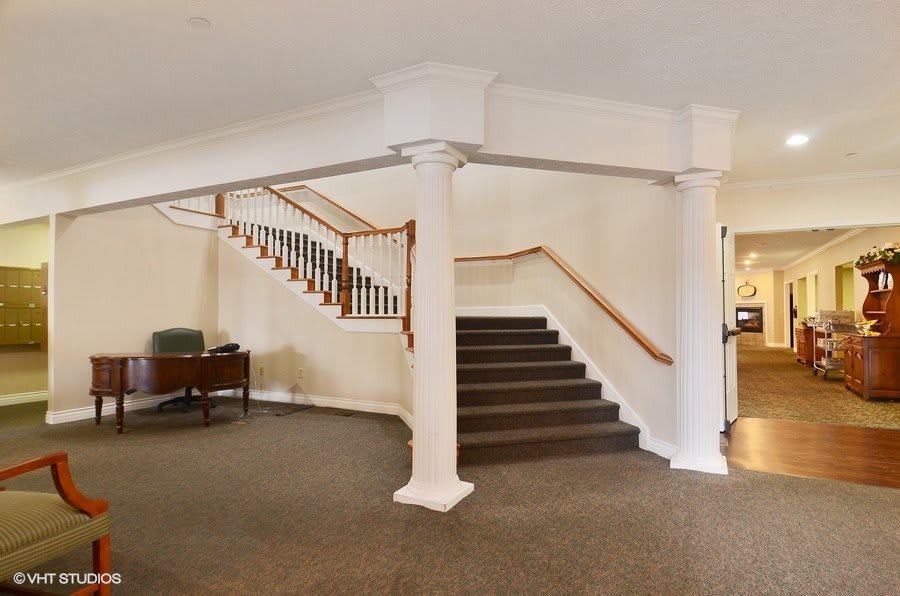 Spacious interior featuring a staircase with elegant columns and carpeted flooring.