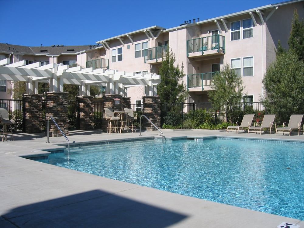 An outdoor swimming pool at an apartment complex, surrounded by balconies and seating areas.