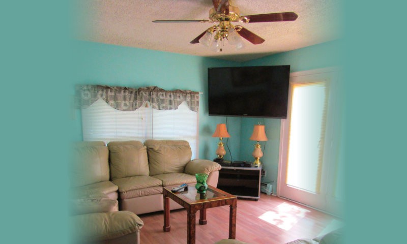 A cozy living room with a sectional sofa, ceiling fan, and a mounted television.