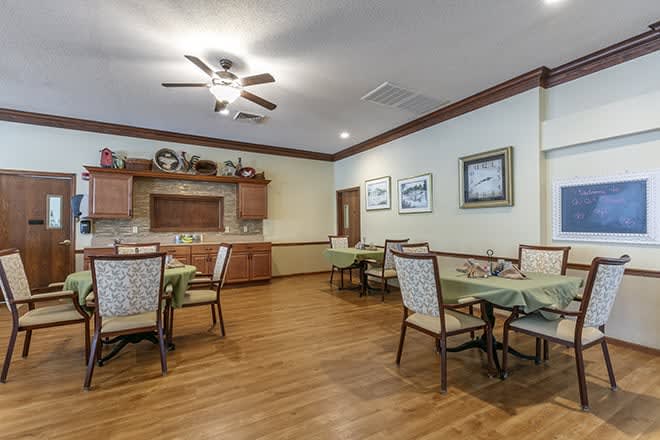 A cozy dining room with neatly arranged tables and chairs, complemented by warm wooden flooring and a ceiling fan.