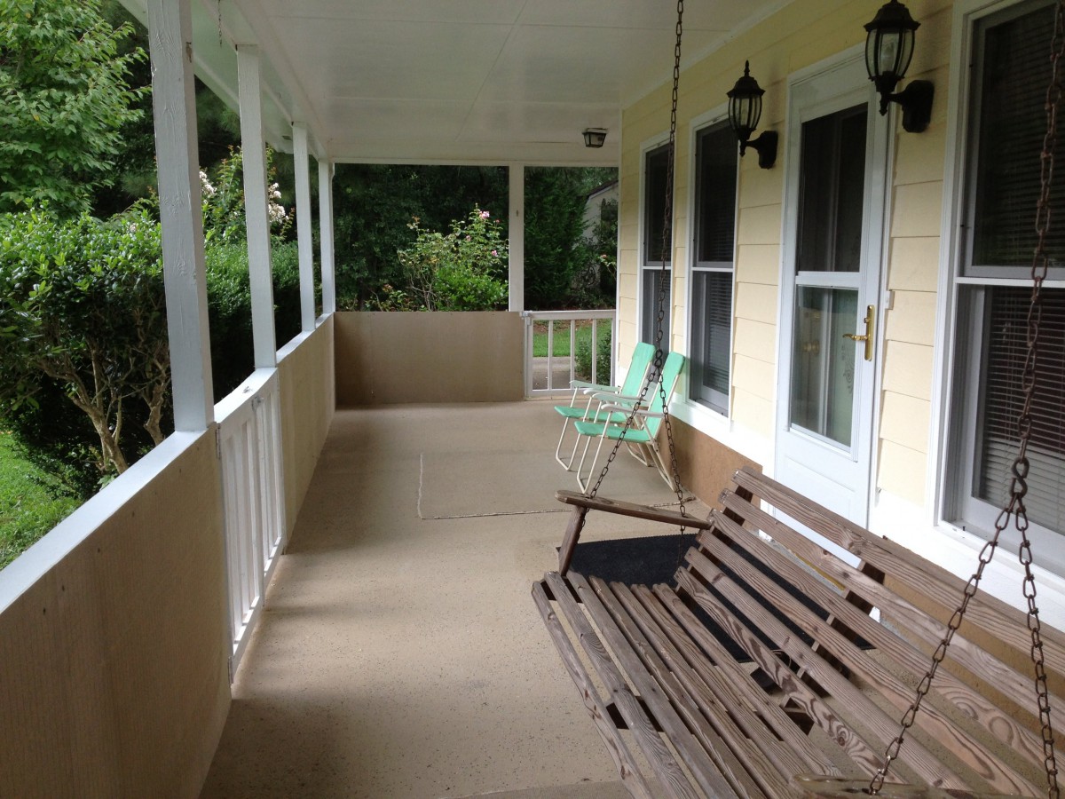 A cozy porch with a swing and chair, surrounded by greenery.