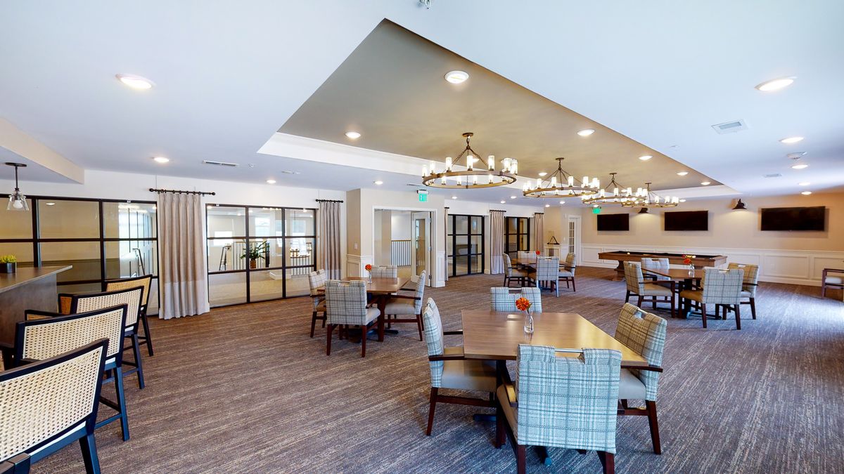 A modern dining area with elegant chandeliers, tables, and chairs on a wooden floor.