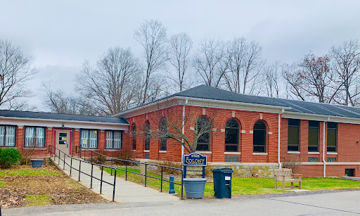 A brick library building with large arched windows, surrounded by trees.