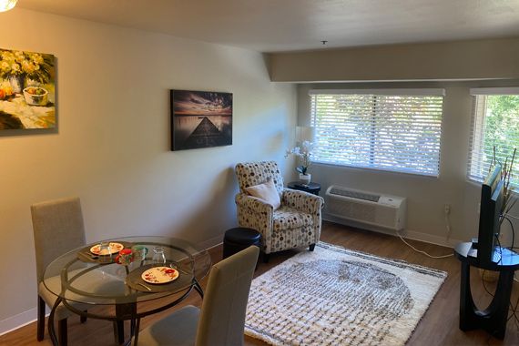 A cozy living room with a glass table, patterned chair, and large window.