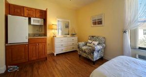 A cozy bedroom with a floral armchair, white dresser, and warm lighting.