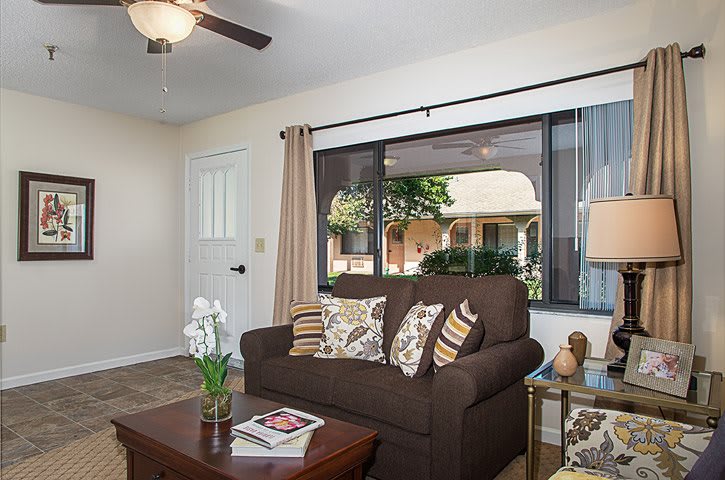 A cozy living room with a brown sofa, decorative cushions, and a coffee table in front of a large window.
