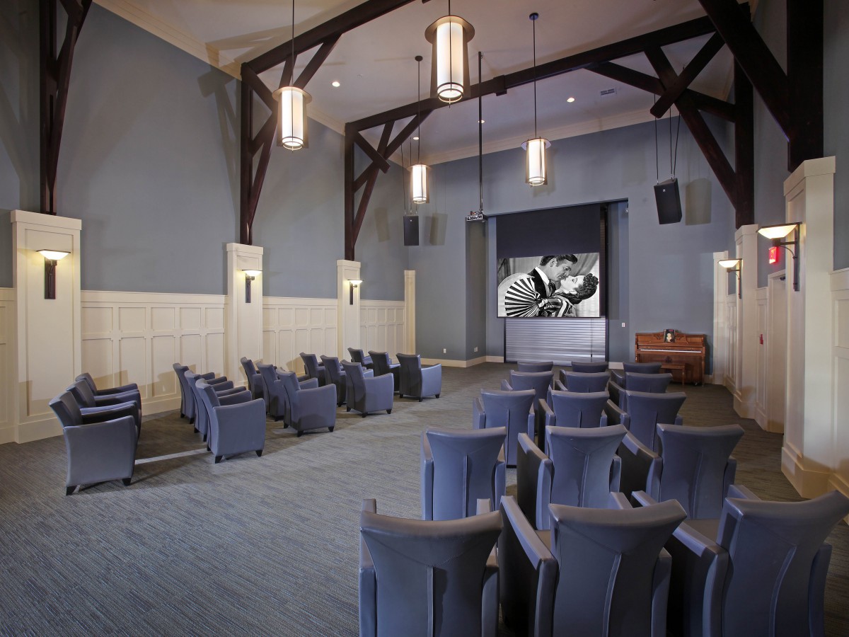 An interior view of a small theater with blue seating facing a stage, featuring modern lighting and architectural beams.