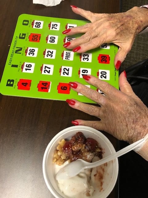 A person with red nail polish is playing bingo while enjoying a bowl of ice cream.