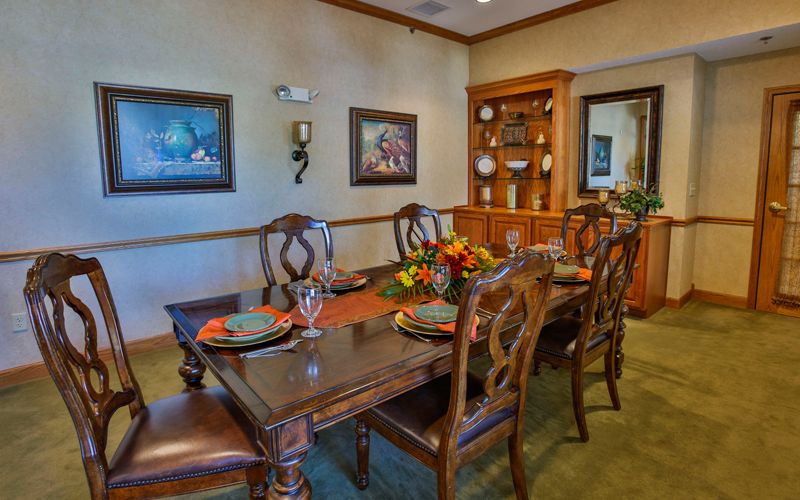 An elegantly set dining room with a wooden table and chairs, adorned with decorative place settings and surrounded by artwork and a china cabinet.