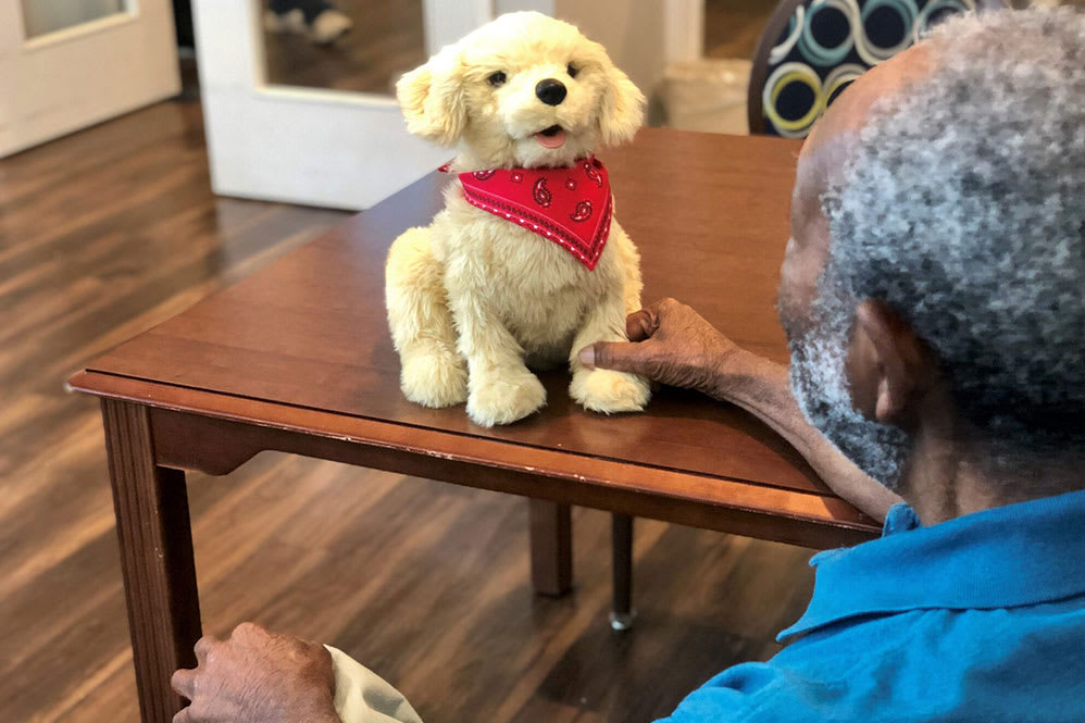 A stuffed toy dog wearing a red bandana sits on a table next to a person.