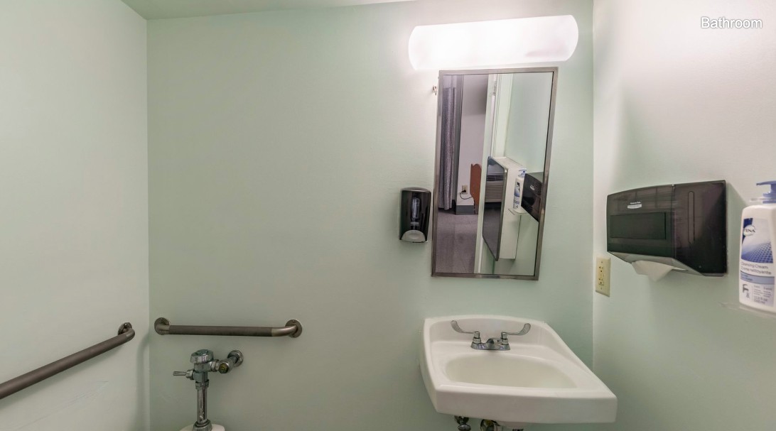 A simple bathroom setup with a sink, mirror, and handrail.